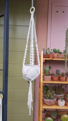 a white macrame hanging from a hook next to potted cacti and succulents