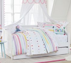 a child's bedroom with white bedding and rainbow colored accessories on the bed