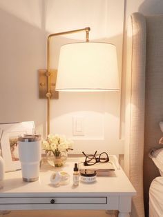 a white table topped with a lamp and eyeglasses next to a vase filled with flowers