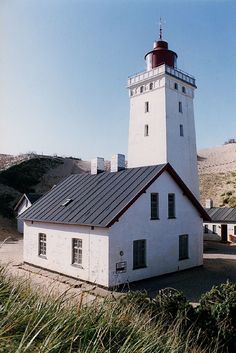 a white building with a red roof and a light house in the middle of it