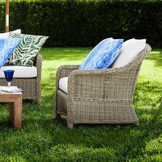 two wicker chairs with blue and white pillows on them sitting in the grass under an umbrella