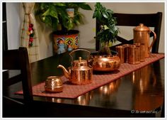 a wooden table topped with copper colored pots and pans next to a potted plant