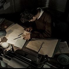 a man sitting at a desk writing on a piece of paper next to an old typewriter