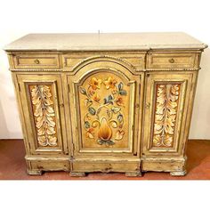 an ornately decorated cabinet with flowers and leaves painted on the front, sitting on a tile floor