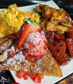 a white plate topped with french toast, strawberries and other breakfast foods next to eggs