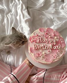 a cat is sniffing a birthday cake with pink frosting and hearts on the top