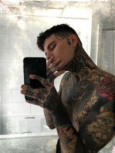 a man with tattoos is looking at his cell phone and holding it up to his face