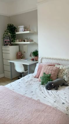 a bed with pink and green pillows in a bedroom next to a white desk area