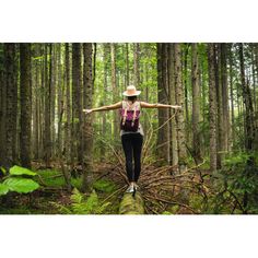 a woman standing on a fallen tree in the woods with her arms spread wide open