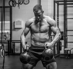 a shirtless man holding two kettles in a gym