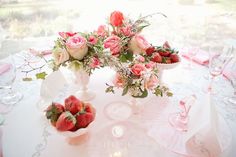 the table is set with pink and white flowers, strawberries, and roses in vases