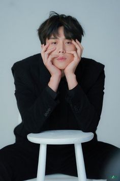 a man sitting on top of a white stool with his hands under his face and looking at the camera