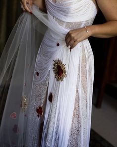 a woman wearing a white dress with red flowers on the side and a veil around her waist