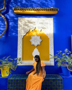 a woman in an orange dress sitting on a blue and yellow wall next to potted plants