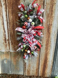 This is a beautifully crafted Christmas-themed centerpiece that is designed to hang on a door. The centerpiece features a lush arrangement of faux greenery and is adorned with a variety of festive decorations, including: - **Ribbons There are large, eye-catching red and white ribbons with festive patterns woven throughout the arrangement. The ribbons are elegantly curled and looped, adding texture and movement. - **Ornaments The centerpiece is embellished with various ornaments in traditional Christmas colors--red, green, and white. These include shiny and matte baubles, as well as fun, candy cane-inspired spiral ornaments. - **Pinecones and Berries There are natural elements like frosted pinecones and red berries, which add a touch of winter to the design. - **Floral Sprays Wispy sprays e Ribbons On Wreaths Christmas, Frosted Pinecones, Christmas Door Swag, Door Wreath Christmas, Wreath Centerpiece, Colorful Decorations, Christmas Door Wreath, Wreath Ornament, Candy Cane Wreath