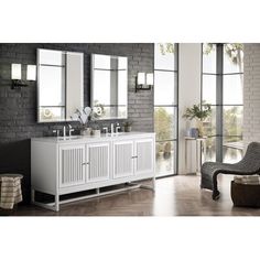 a white bathroom vanity with two sinks and mirrors in front of a brick wall behind it