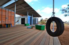 there is a tire hanging from a swing on the deck outside an orange container house