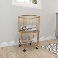 a yellow wire basket on wheels in the corner of a room with white walls and wood flooring