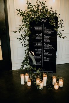 a table with candles and greenery next to a black sign that says wedding seating