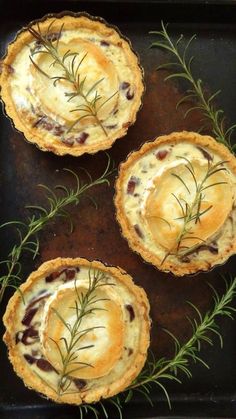 three small tarts on a baking sheet with some rosemary sprigs around them