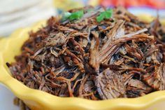 a yellow bowl filled with shredded meat on top of a table