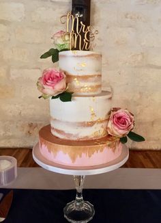 a three tiered cake with pink flowers on top sits on a table in front of a brick wall