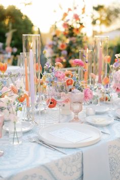 the table is set with candles, plates and vases filled with flowers on it