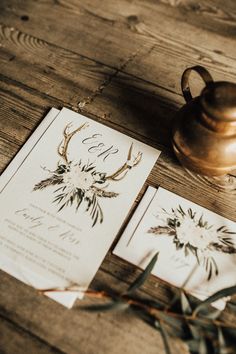 wedding stationery with antlers and flowers on it next to a copper teapot