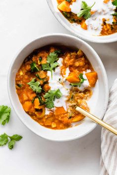 two white bowls filled with soup and garnished with cilantro, sour cream and parsley