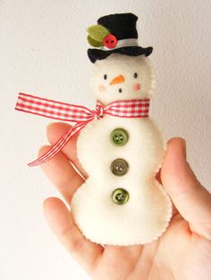 a hand holding a small snowman made from buttons