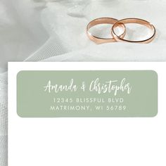 two wedding rings sitting on top of a white envelope with the words amanda and christopher