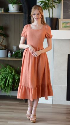 "Meet the Villanelle Dress! A lovely peach dress with cottage-core style and a unique kind of wild elegance. With gently puffed sleeves, a ruffled hem, and soft textured fabric that is extremely light and gorgeously flowy, consider this dress perfect for frolicking.  All Poet dresses come with a cardstock poem delivered in a wax-sealed envelope. 🪶  Custom design by Poet Zipper in the back Midi-length skirt Square neck Dress length (length may vary slightly with size variant): -Waist to hem: 32.5 in -Shoulder to hem: 48 in Care instructions: -Machine washable -Air-dry for longest life -Iron on low heat when necessary Models: -Chloe: Size XL | 5'4\" -Jenna: Size S | 5'9\" Fabric: 80% Rayon 20% Nylon" Spring Prairie Dress With Puff Sleeves And Ruffle Hem, Cottagecore Dress With Ruffle Hem And Puff Sleeves, Cottagecore Square Neck Dress With Ruffle Hem, Cottagecore Prairie Dress With Puff Sleeves And Ruffles, Peach Ruffled Midi Dress For Garden Party, Fitted Cottagecore Midi Dress With Ruffles, Cottagecore Fitted Midi Dress With Ruffles, Cottagecore Midi Dress With Ruffles And Square Neck, Cottagecore Puff Sleeve Dress With Square Neck And Ruffles