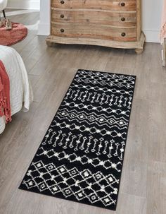 a black and white rug on the floor in a room with wooden dresser, bedding and chest of drawers