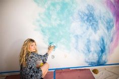 a woman is painting a wall with blue and pink paint