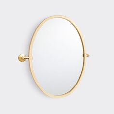 an oval mirror mounted on the wall with a gold frame and metal fittings is shown