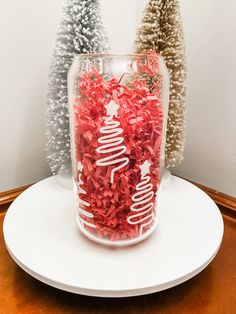 a glass with red shredded paper in it sitting on a table next to christmas trees