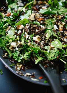 a close up of a plate of food with greens and nuts on it next to a spoon