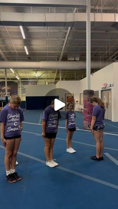 three girls in purple shirts are standing on a blue floor and talking to each other