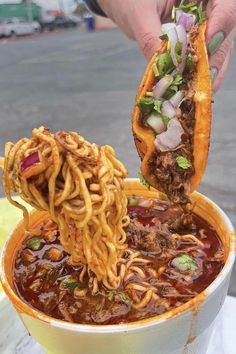 a person is eating noodles with chopsticks in a bowl on a table outside