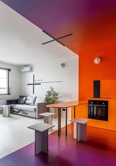 a living room filled with furniture and an orange wall behind the couch is a dining table