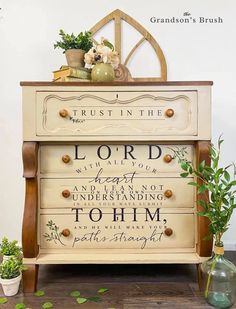 a white dresser with words painted on it and plants in vases next to it