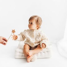 a baby is sitting on a pillow while someone holds a star wand in their hand