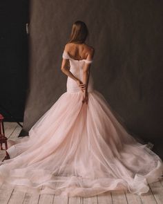 a woman in a pink dress standing on a wooden floor with her back turned to the camera