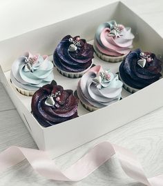 six cupcakes in a white box with pink, blue and purple frosting