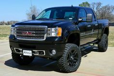 a black truck parked in a parking lot next to a grass covered field and trees