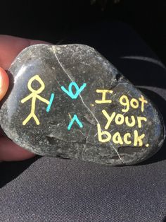 a person holding a rock with writing on it that says i got your back and two stick figures drawn on it