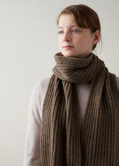 a woman wearing a brown scarf standing in front of a white wall