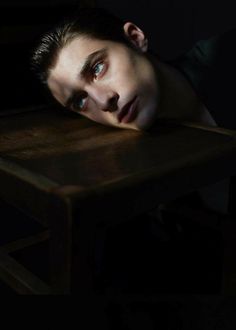 a young man sitting at a table with his head resting on the top of it