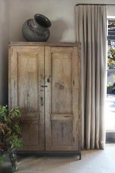 an old wooden cabinet sitting next to a window in a room with curtains and potted plants