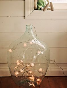 a glass vase filled with lights sitting on top of a wooden floor next to a window